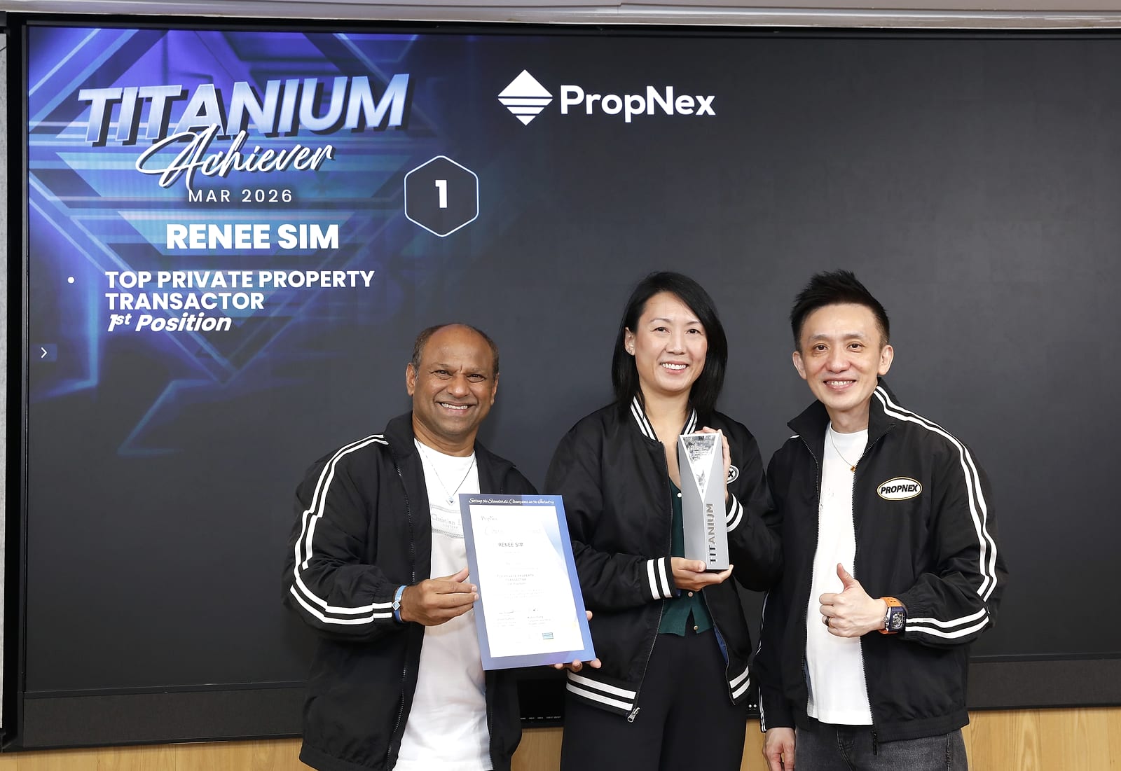Renee Sim holding a Titanium trophy and a certificate on stage at PropNex, flanked by two PropNex leaders, with a screen behind reading "Titanium Achiever, March 2026, Renee Sim, Top Private Property Transactor, 1st Position".